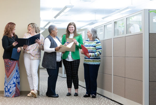 Homepage - Strate Insurance Group Team Smiling and Talking While Holding Folders with Documents as They Stand in the Hallway of their Brightly Lit Office